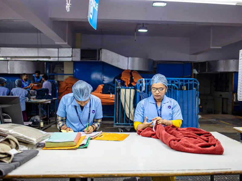 Two workers in a textile factory sorting fabric at a table under bright lighting