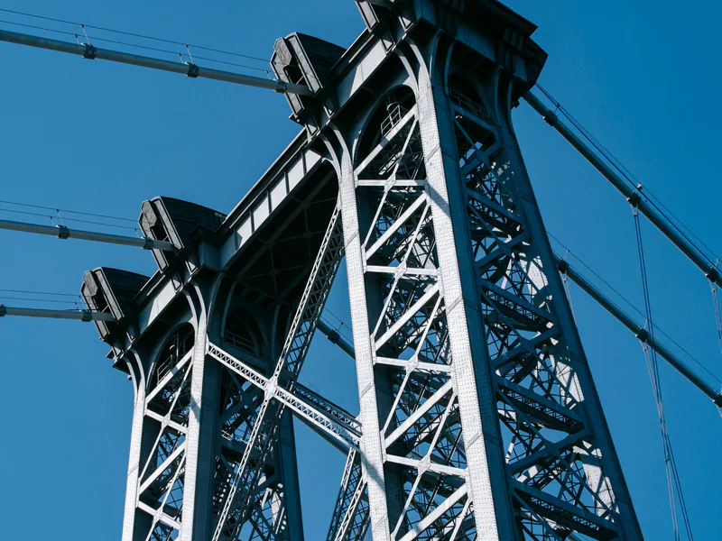 From below of suspension Williamsburg Bridge with long metal constructions against cloudless sky