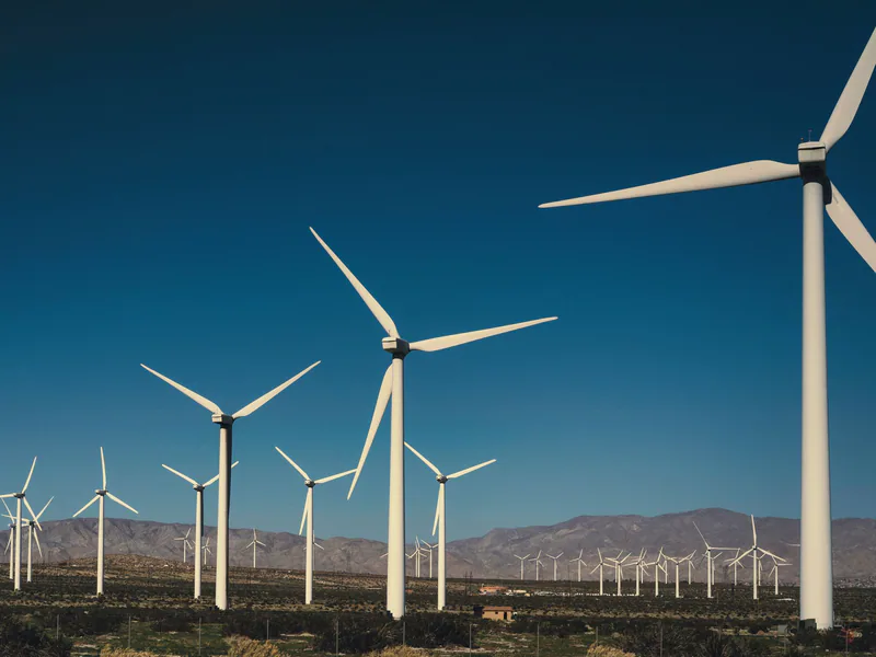 A vast landscape of wind turbines generating clean energy with a backdrop of mountains and a clear blue sky