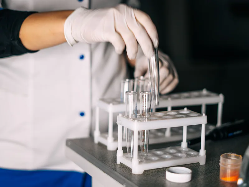 A scientist in a lab coat handling test tubes in a laboratory setting with a focus on equipment