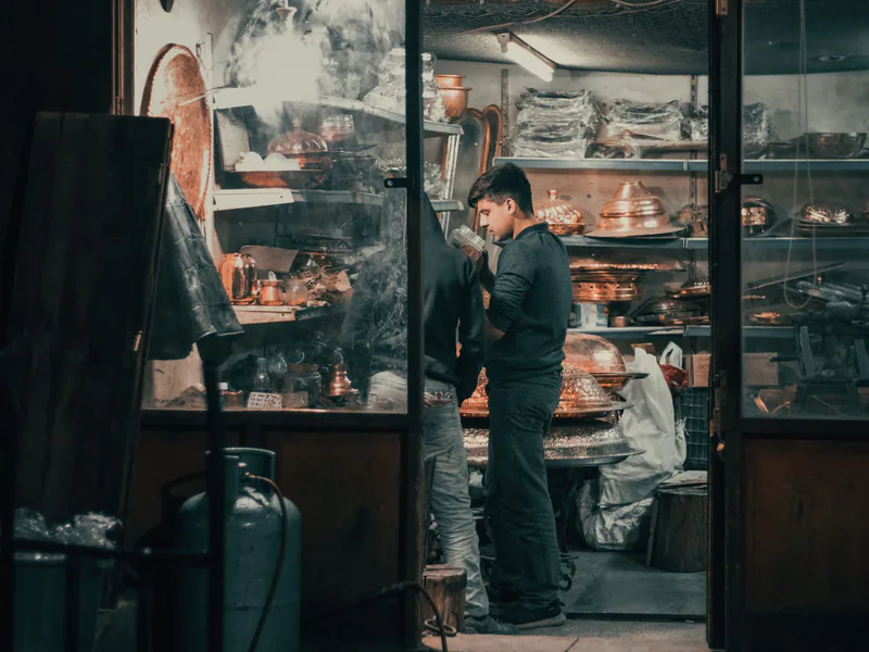 Side view of young ethnic male seller working in local souvenir shop and offering client various goods