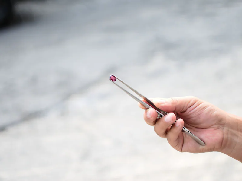 Close-up of a hand holding a gemstone with tweezers outside, highlighting precision and detail