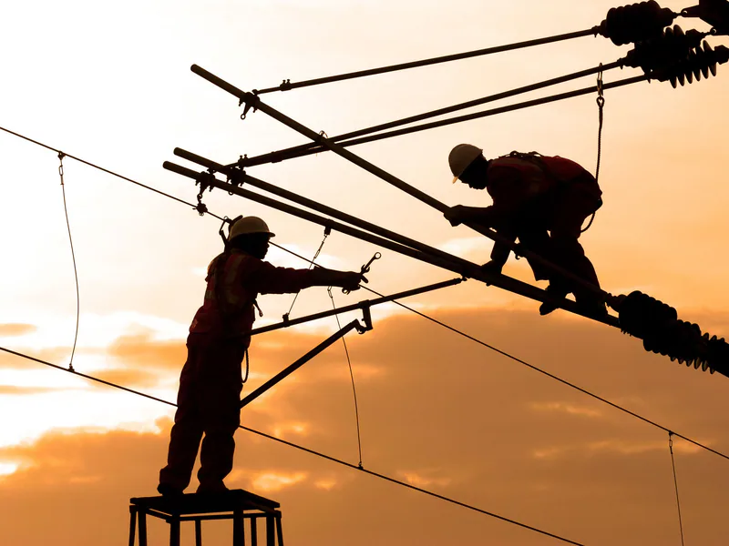 Electricians repairing power lines at sunset, showcasing teamwork and safety