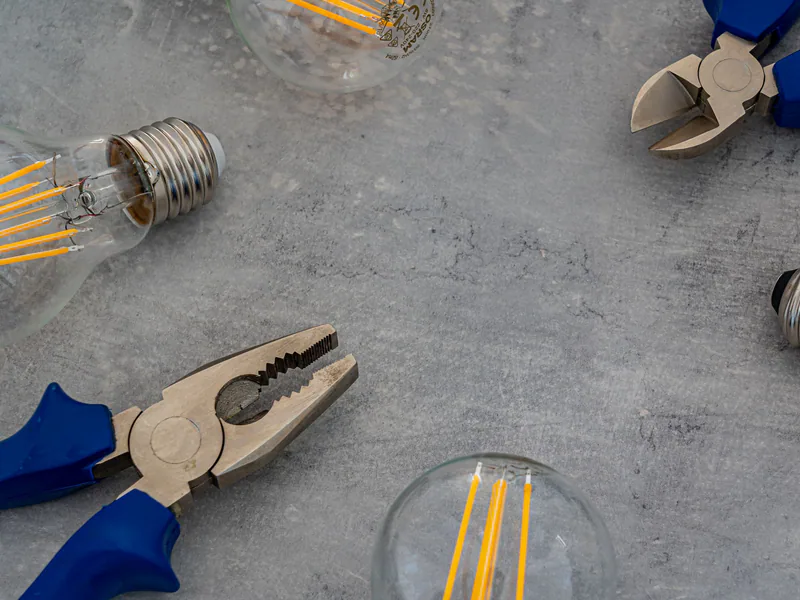 Top view of Edison bulbs and blue-handled pliers arranged on a gray concrete surface
