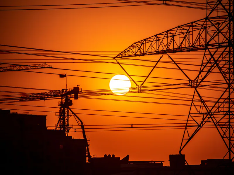 Dramatic sunset over Dubai with silhouetted pylons and cranes against an orange sky