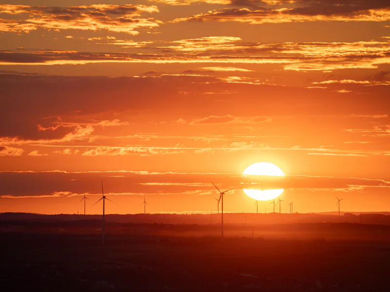 Stunning sunset over wind turbines near the sea with a glowing orange sky