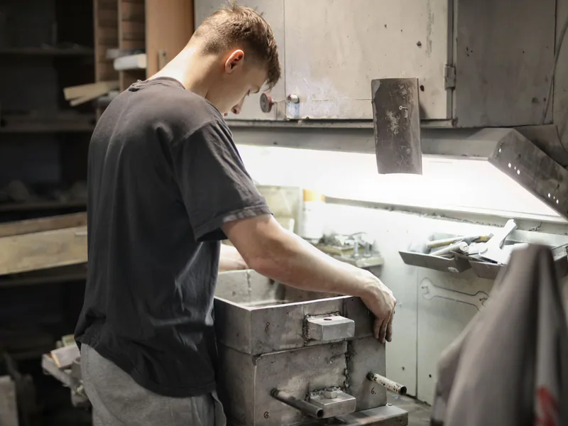 Side view of junior fitter attentively examining metal detail on workbench in workshop