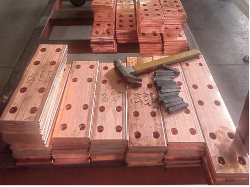 Stacks of punched copper busbar parts beside CNC processing equipment