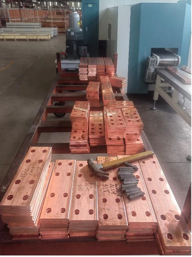 Punched copper busbar parts stacked on a workbench showing material yield and hole patterns